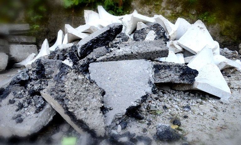 Ein Haufen Schutt, einschließlich grauer Beton und weißer Materialien, verstreut auf dem Boden mit einer moosbewachsenen Wand im Hintergrund.