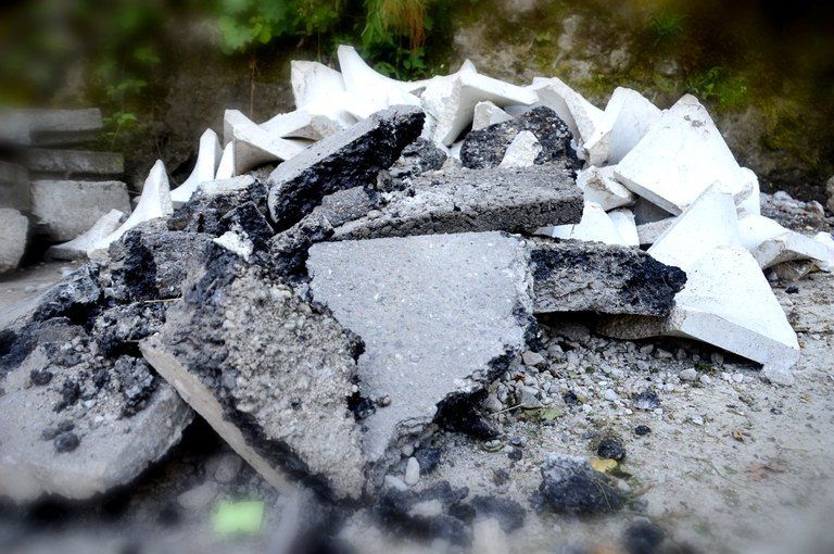 Ein Haufen Schutt, einschließlich grauer Beton und weißer Materialien, verstreut auf dem Boden mit einer moosbewachsenen Wand im Hintergrund.
