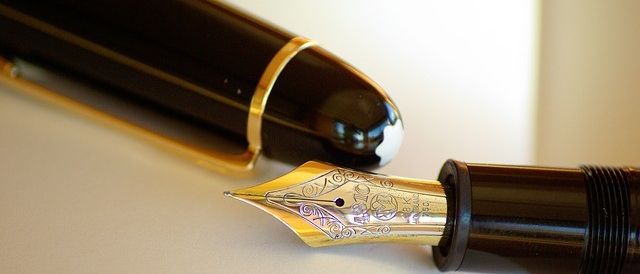 Nahaufnahme eines schwarzen und goldenen Füllfederhalters mit einer Feder, die auf einem offenen Buch ruht.