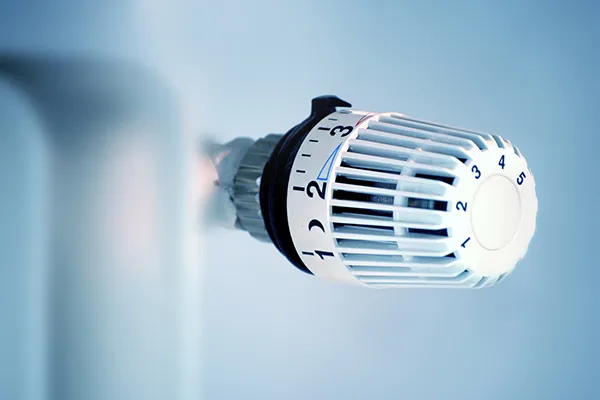 Ein Nahaufnahme eines weißen Thermostats mit einem blauen Pfeil, der auf die Nummer 2 auf einer Skala von 1 bis 5 zeigt.