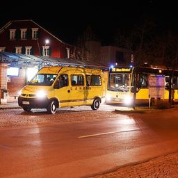Eine Bushaltestelle bei Nacht mit zwei Bussen, einem gelben mit eingeschalteten Lichtern und einem geparkten.