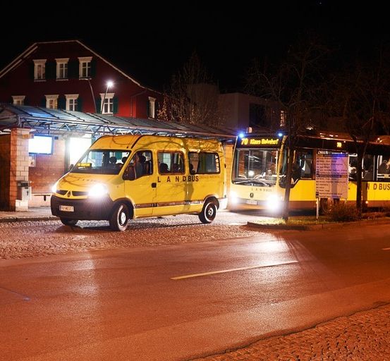 Eine Bushaltestelle bei Nacht mit zwei Bussen, einem gelben mit eingeschalteten Lichtern und einem geparkten.
