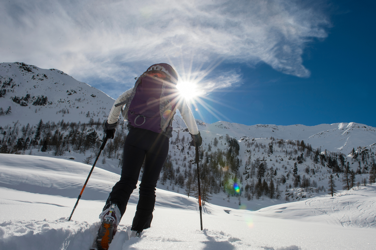 Eine Person, die in verschneiten Bergen Langlauf betreibt, mit einer hellen Sonne am Himmel.
