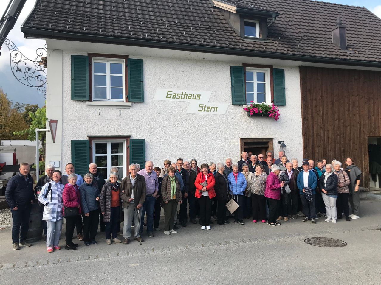 A group of people stands in front of a building named Gasthaus Stern. The building has green shutters and a wooden door. The people are dressed for cooler weather.