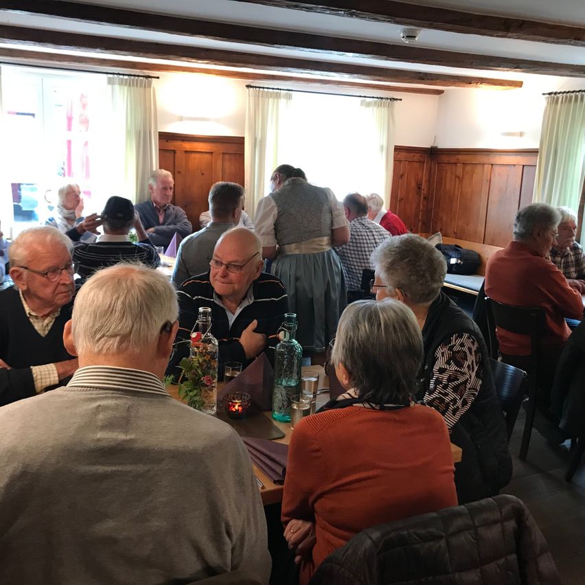 A group of elderly people are sitting around a table in a restaurant. They are all wearing glasses. There are two bottles and a candle on the table.