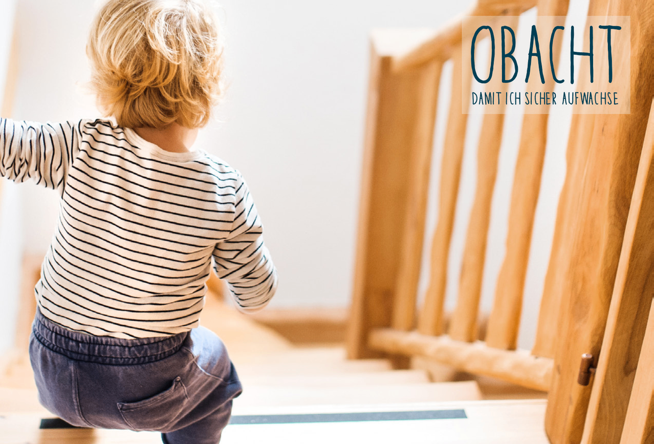 A child with blonde hair wearing a striped shirt and pants is climbing up a staircase.