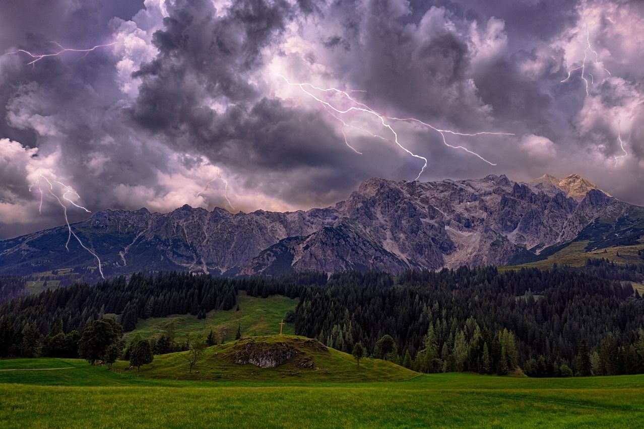 Eine dramatische Landschaft mit einem stürmischen Himmel, der von Blitzen erleuchtet wird und die Bergkette darunter beleuchtet.