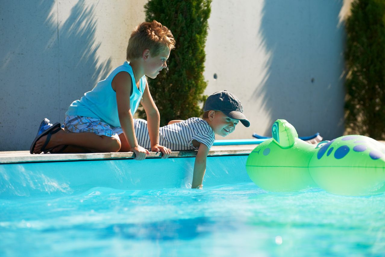 Zwei Jungen spielen im Pool. Ein Junge greift nach einem schwimmenden Frosch, während der andere zuschaut.