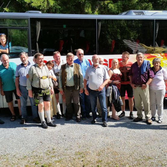 Eine Gruppe von Menschen posiert für ein Foto vor einem bunten Bus. Ein Mann trägt ein traditionelles Outfit.
