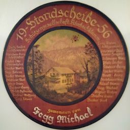 Rundplakette mit '19 Stardscheben 56' in Gold. Ein Haus in der Mitte, umgeben von Bäumen und Bergen. Namen wie 'Egg Michael' sind in Weiß um den Rand herum geschrieben.