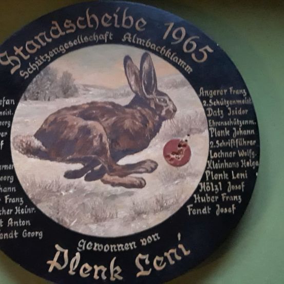 Eine runde Plakette der Almbachklamm Jagdgesellschaft aus dem Jahr 1965 zeigt einen Hasen und einen angeknabberten Apfel. Namen und Rollen sind um das Bild herum eingraviert.
