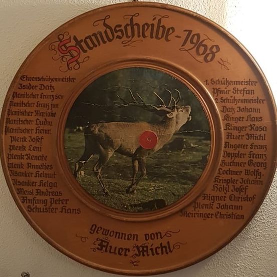Eine kreisförmige Holzplakette mit einem Bild von einem Hirsch. Sie hat die Aufschrift 'Standscheibe-1968' oben. Namen sind auf Deutsch um den Kreis herum geschrieben.