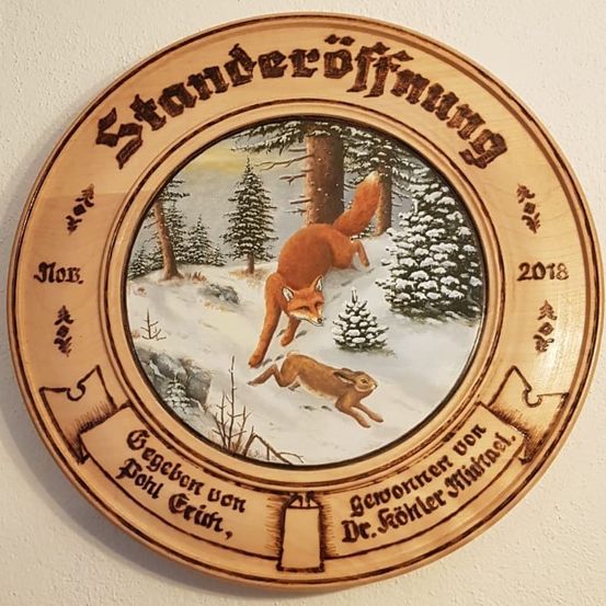 Eine hölzerne runde Plakette zeigt einen Fuchs und einen Hasen in einem verschneiten Wald. Es steht 'Ständeröffnung' und '2018'. Darunter befindet sich ein Band mit 'Gegeben von Pohl, Gruft' und 'Gewormer von Dr. Kohler Michael'.