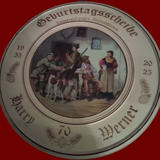 Eine Gedenkplatte mit einer Szene von Menschen, die um einen Tisch versammelt sind, datiert auf 1935. Es zeigt einen Mann mit Gewehr, eine sitzende Frau und zwei stehende Männer. Die Platte hat einen roten Hintergrund mit goldenen Verzierungen.