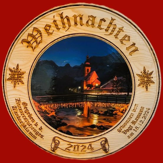 Ein weihnachtlicher Holzschmuck mit einem Foto einer kleinen Stadt bei Nacht. Das Foto zeigt eine Brücke über einen Fluss und eine Kirche im Hintergrund. Der Schmuck hat die Wörter 'Weihnachten' und das Jahr '2024'.