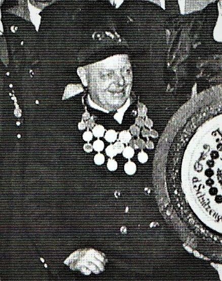 Ein formelles Foto eines älteren Mannes in Uniform mit Orden, der sitzt und lächelt, mit einem Kuchen vor ihm.