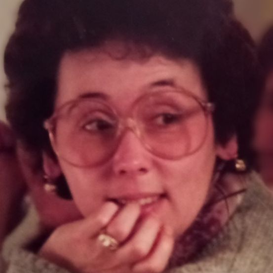 Eine Frau mit kurzem schwarzem Haar, die eine Brille und einen Ring trägt und ihr Kinn mit der linken Hand hält.