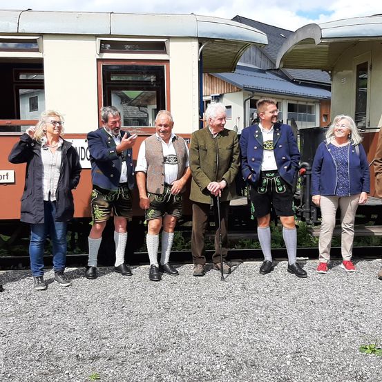 Eine Gruppe von Menschen, darunter zwei Frauen und vier Männer, steht vor einem Zug. Sie alle lächeln und scheinen für ein Foto zu posieren.