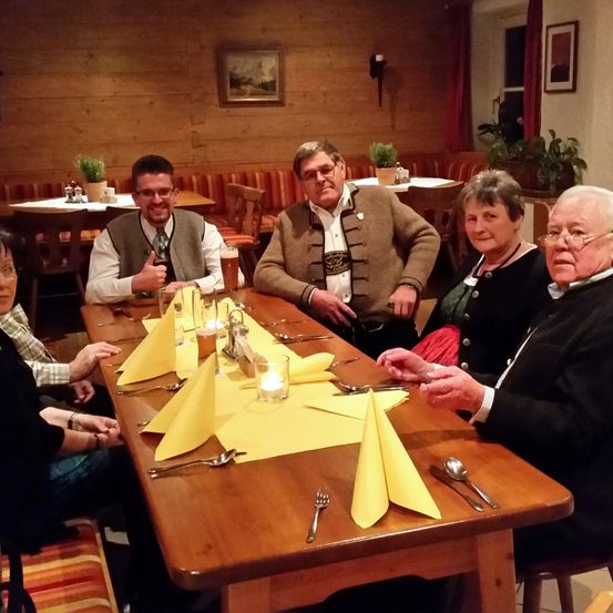 Eine Gruppe von Menschen sitzt an einem Tisch in einem Restaurant. Sie tragen alle eine Brille. Auf dem Tisch liegen gelbe Servietten.