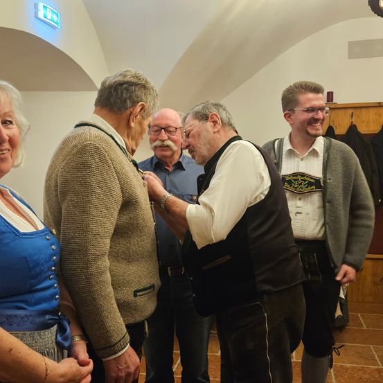Eine Gruppe von Menschen in einem Raum, ein Mann erhält eine Medaille von einem anderen Mann, während eine Frau und zwei andere Männer zusehen.