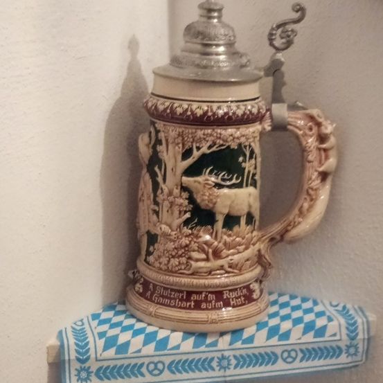 Ein dekorativer Bierkrug mit Hirsch- und Waldszene, auf einem blau-weiß karierten Tuch platziert.