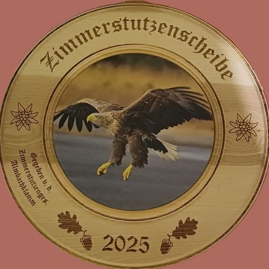 Eine hölzerne Plakette mit einem fliegenden Adler, dem Jahr 2025 und dekorativen Blättern. Der Hintergrund ist grau mit verschwommenem Effekt. Der Text lautet 'Zimmerstutzenscheide'.