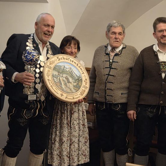 Fünf Menschen stehen lächelnd und halten einen Teller mit einem Bild. Der Mann auf der linken Seite hält einen Pokal. Auf dem Teller steht Schutzenschonhaus 2026.