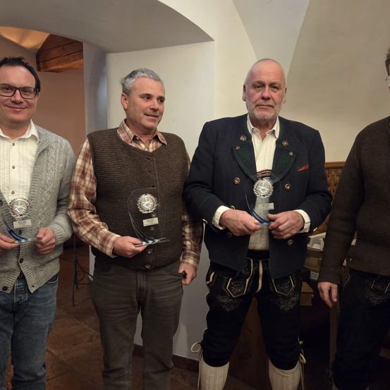 Vier Männer stehen in einem Raum, halten Auszeichnungen in der Hand, lächeln und posieren für ein Foto. Der Mann in der Mitte trägt einen Anzug.