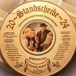 Eine kreisförmige Holzplakette zeigt ein Foto von vier Männern mit den Worten '20. Standscheibe 24'. Namen von Personen sind in zwei Spalten aufgeführt. Die Plakette ist auf den 28. Februar 2024 datiert.