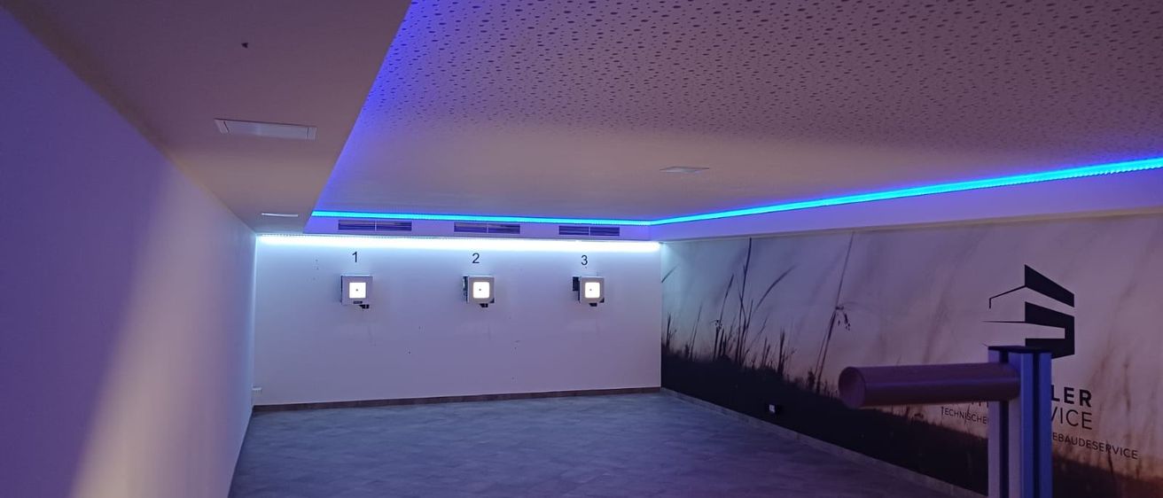 Ein leerer Raum mit weißen Wänden und einer lila Decke. Drei nummerierte Paneele sind an der Wand montiert. Ein landschaftliches Wandbild schmückt die rechte Wand.