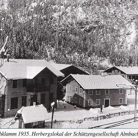Ein Schwarz-Weiß-Foto von 1935 zeigt mehrere schneebedeckte Gebäude, mit einer Person, die in der Nähe eines davon geht.