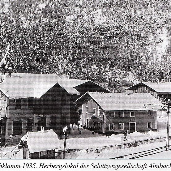 Ein Schwarz-Weiß-Foto von 1935 zeigt mehrere schneebedeckte Gebäude, mit einer Person, die in der Nähe eines davon geht.