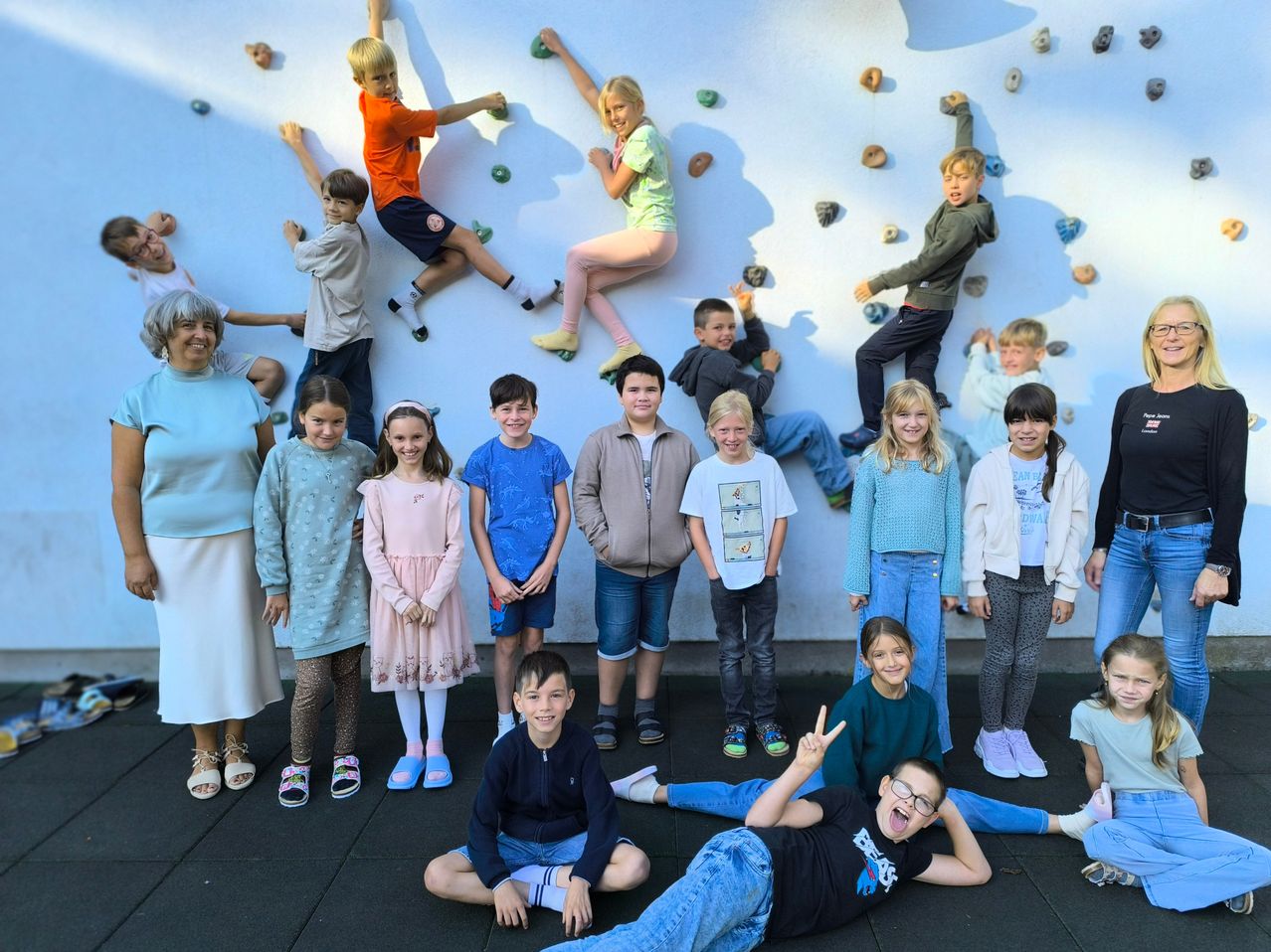 Eine Gruppe von Kindern und Erwachsenen posiert für ein Bild vor einer Kletterwand. Einige Kinder klettern an der Wand, während andere auf dem Boden posieren.