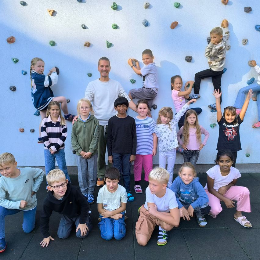 Eine Gruppe von Kindern, einige kniend und andere kletternd, posiert für ein Foto vor einer Wand mit Klettergriffen.