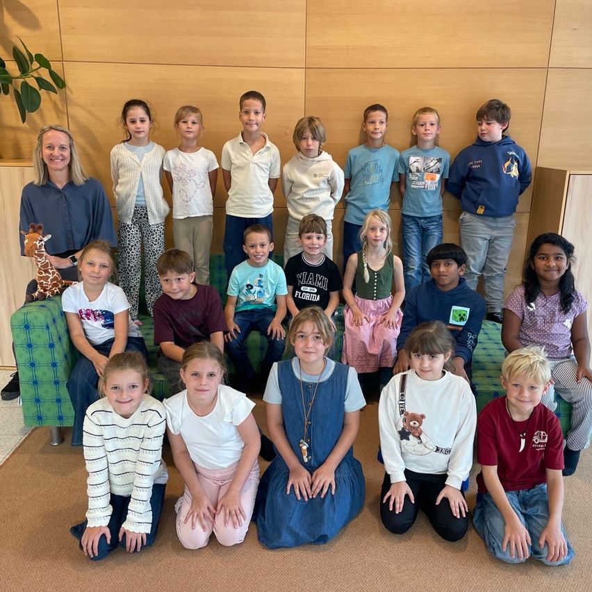 Eine Gruppe von Kindern und einer erwachsenen Frau posiert für ein Foto in einem Raum mit einer Holzwand und einer grünen Couch.