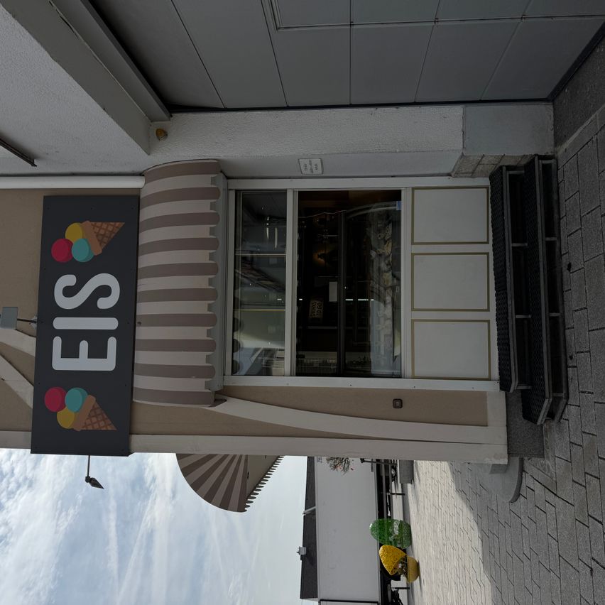 Eine Eisdiele mit einem Schild mit der Aufschrift EIS, das drei Eisbecher zeigt, vor einem Fenster.