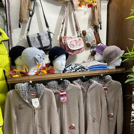 Ein Bekleidungsgeschäft zeigt Hüte und Jacken an Mannequins und einer Wand. Die Jacken sind braun mit verschiedenen Designs, und die Hüte sind auf einem Regal ausgestellt. Einige Handtaschen hängen auch an der Wand.