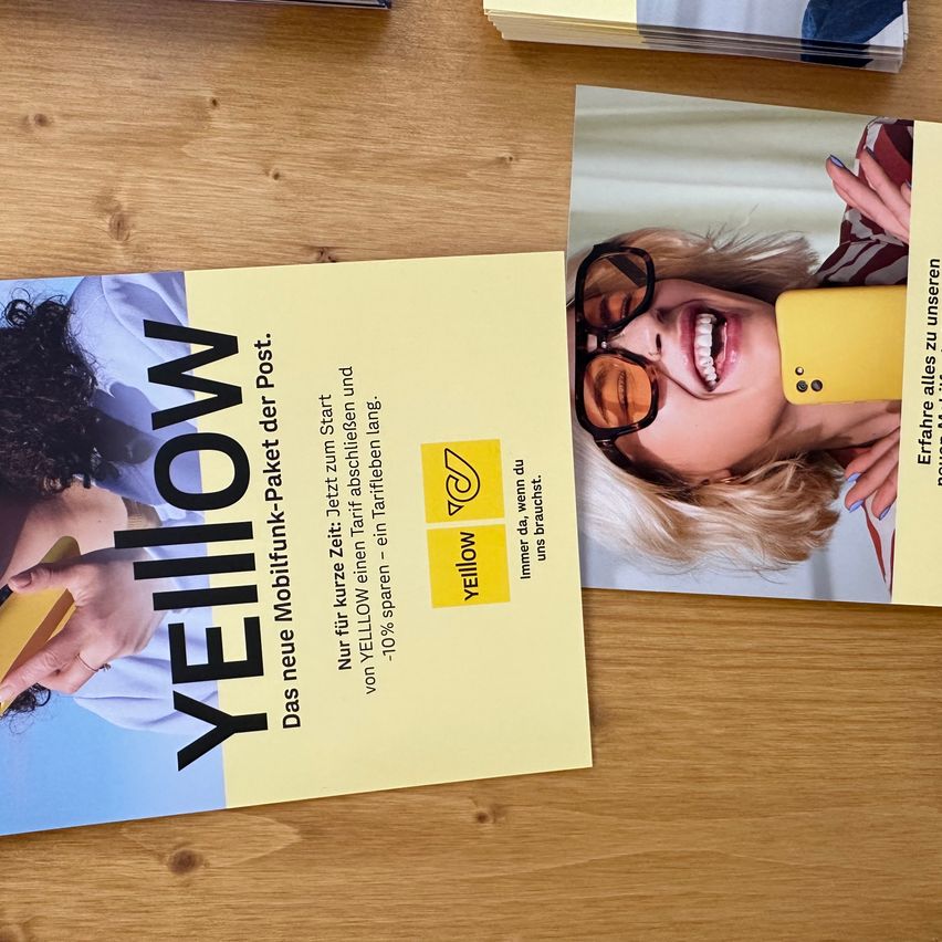 A yellow business card on a wooden table with a woman holding a phone. The card reads 'YELLOW' in bold letters and includes an offer for a 10% discount.