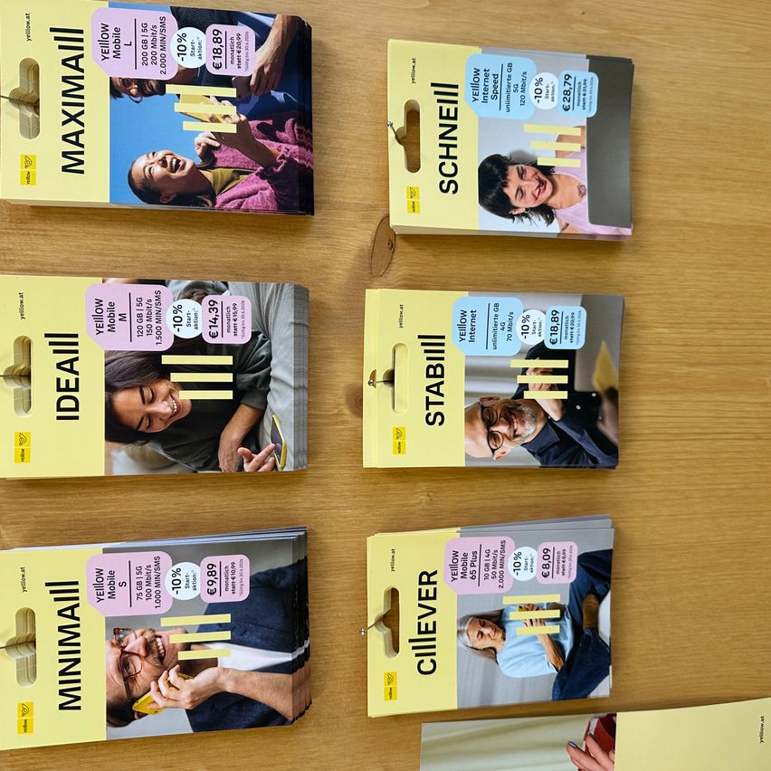 Multiple mobile phone plan packages displayed on a wooden surface. Each package has a different name like 'Maximall', 'Schneill', 'Stabil', 'Ideall', 'Minimall', and 'Cliever'. They all feature a person in a colorful shirt.