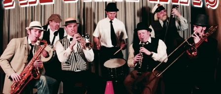 A group of musicians dressed in vintage attire, playing various instruments such as saxophones, trumpets, and trombones. The image is set against a backdrop with the text 'Dixieland Swing Hot Jazz'. The date and time of the event are also displayed.
