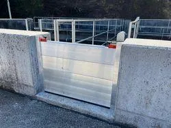 Eine Betonwand mit einem weißen Rolltor ist zu sehen. Das Tor ist geschlossen, und die Betonwand hat zwei rote Reflektoren. Hinter dem Tor befindet sich ein Metallgeländer.