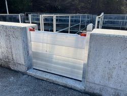 Eine Betonwand mit einem weißen Rolltor ist zu sehen. Das Tor ist geschlossen, und die Betonwand hat zwei rote Reflektoren. Hinter dem Tor befindet sich ein Metallgeländer.