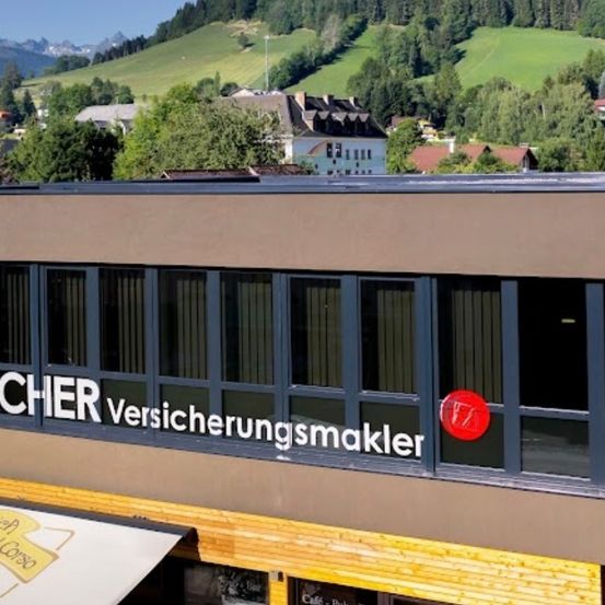 Ein Gebäude mit dem Namen Bacher Versicherungsmakler wird gezeigt. Im Hintergrund ist eine Bergansicht zu sehen. Die Fenster haben Jalousien.