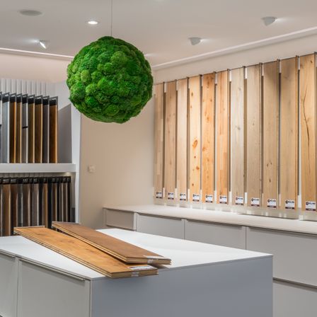 Ein moderner Raum mit verschiedenen Holzpaneelen, einer hängenden grünen Mooskugel und Holzbrettern auf einer Arbeitsplatte.