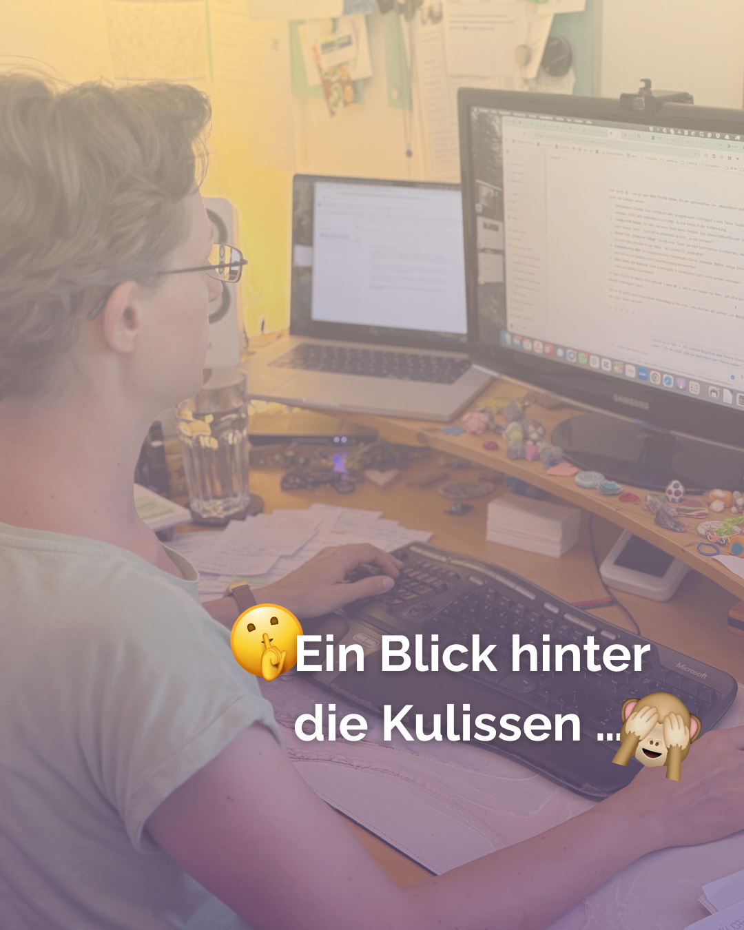 Eine Frau mit Brille arbeitet an einem Computer, mit einem Glas Wasser und einer Tastatur auf dem Schreibtisch. Der Computerbildschirm zeigt Text und Emojis an.