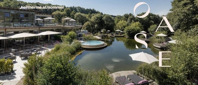 Luftaufnahme eines Resorts mit Pool, umgeben von Bäumen und Sonnenschirmen. Ein Website-Link ist sichtbar.