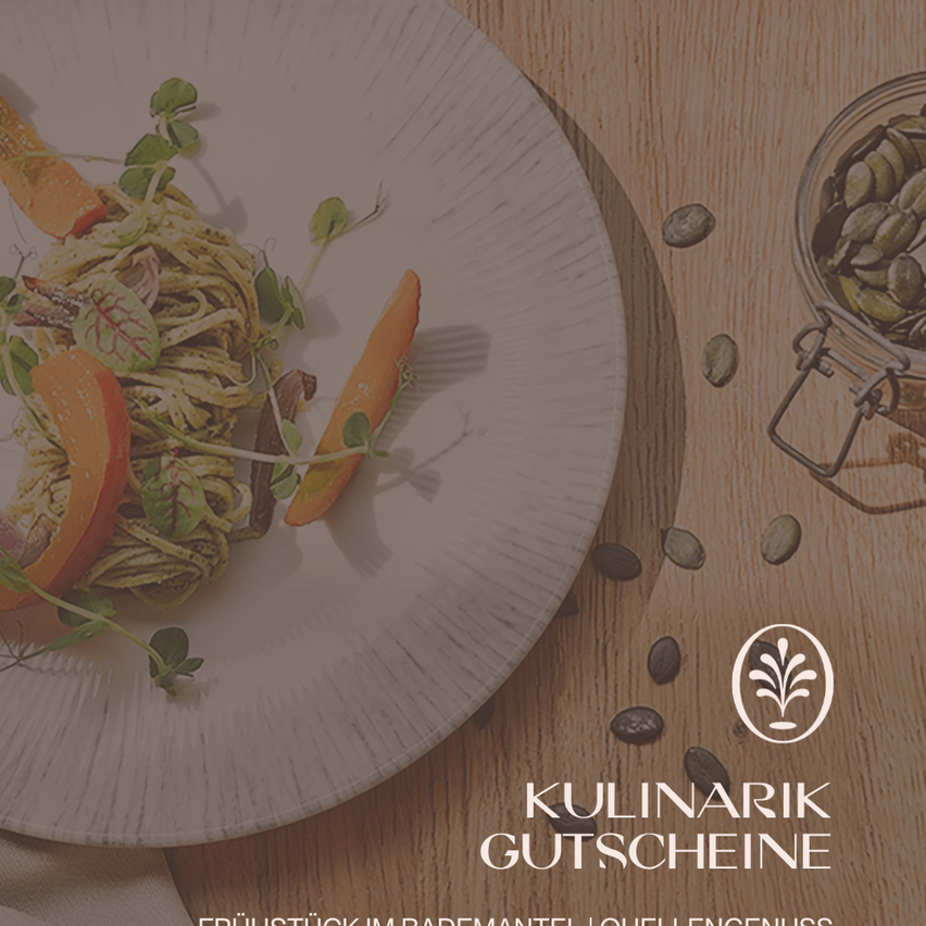 Ein Teller mit Pesto-Pasta, orange Karotten und Microgreens steht auf einer Holzoberfläche. In der Nähe ist ein Glas mit Samen und ein Logo zu sehen.