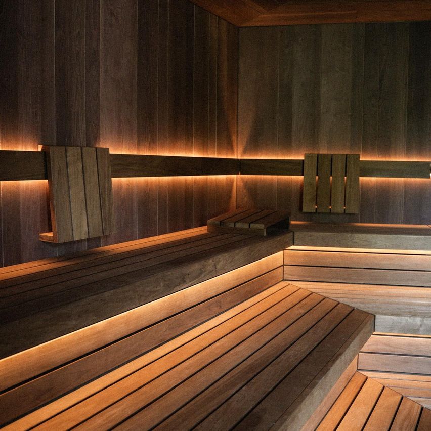 Ein leerer Holzsaunaraum mit Holzbänken und Wänden, beleuchtet von warmem, ambientem Licht.