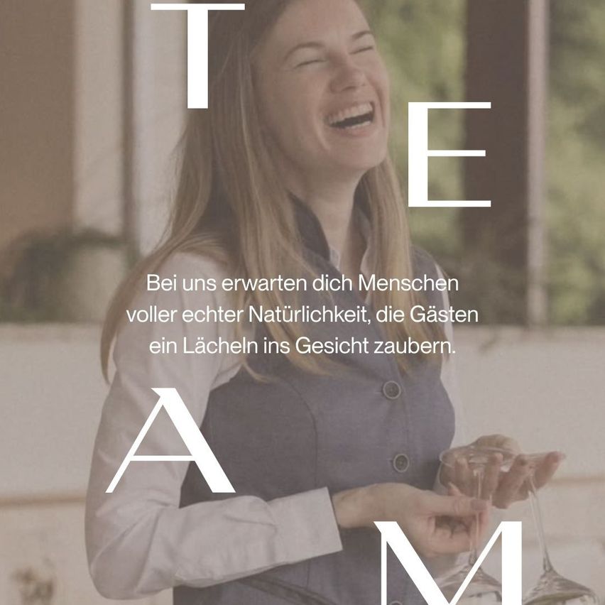 A smiling woman holding a wine glass, surrounded by the letters T, E, A, M. She is wearing a gray vest and a white shirt. Behind her, a blurred background with a plant and a window.