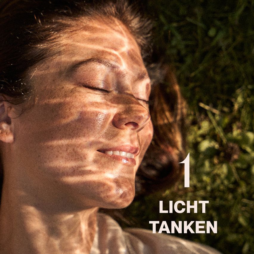 Eine Frau mit geschlossenen Augen liegt auf Gras, beleuchtet von Sonnenlicht, mit den Worten '1 LIGHT TANKEN' in der unteren rechten Ecke.
